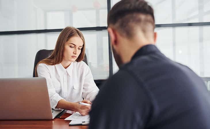 woman writing papers while talking to a man in an office