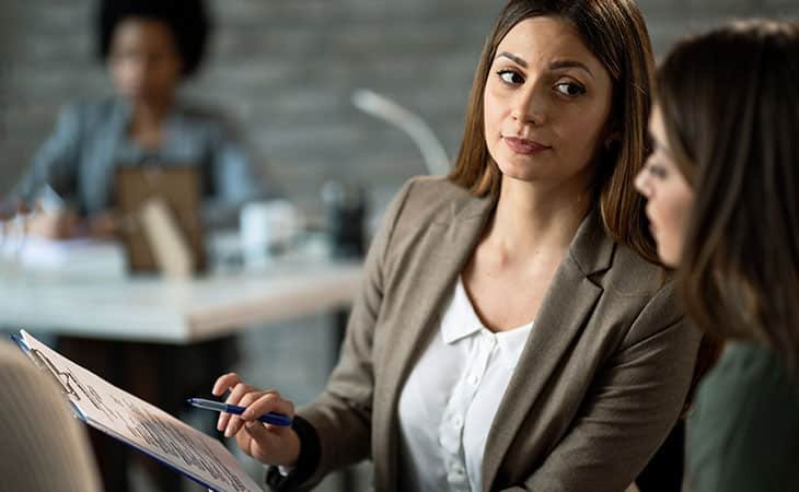 woman looking at a woman and pointing papers